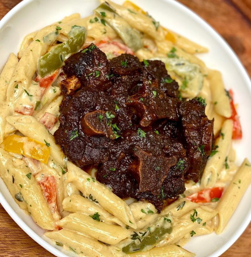 Fresh ingredients for slow-braised oxtail pasta recipe including oxtails, vegetables, and herbs arranged on marble counter